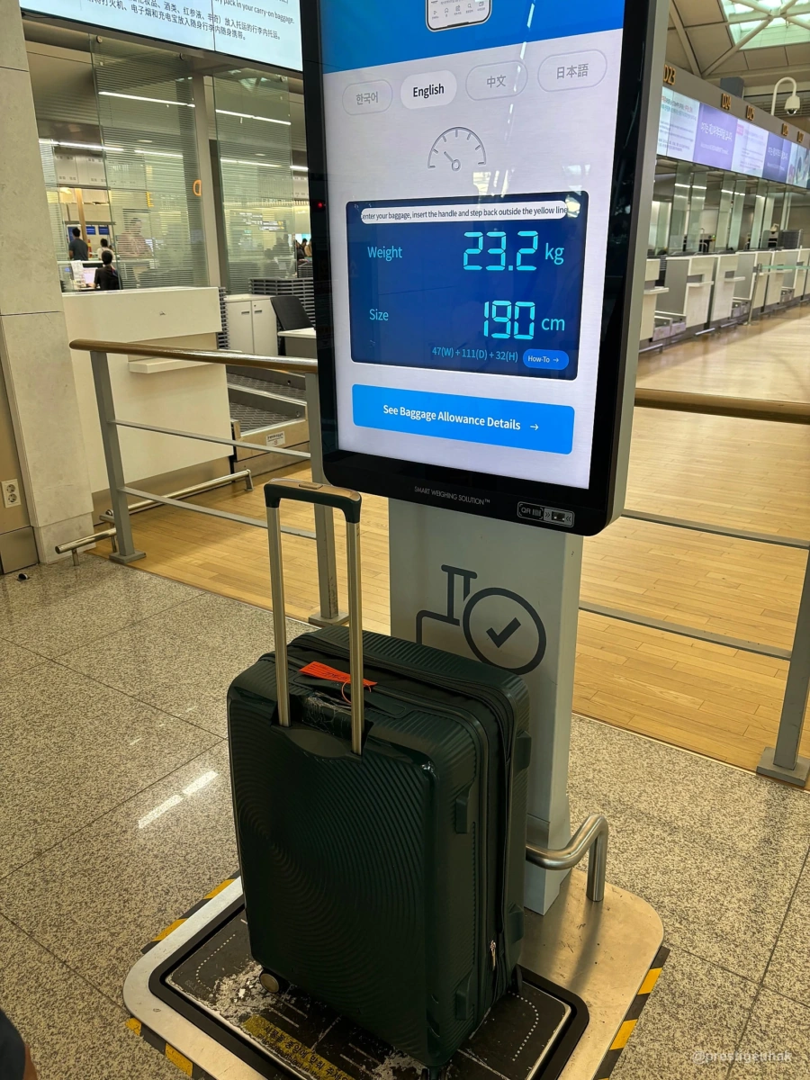 공항 수하물 측정대에 세운 짙은색 여행 가방과 무게·크기 표시 화면